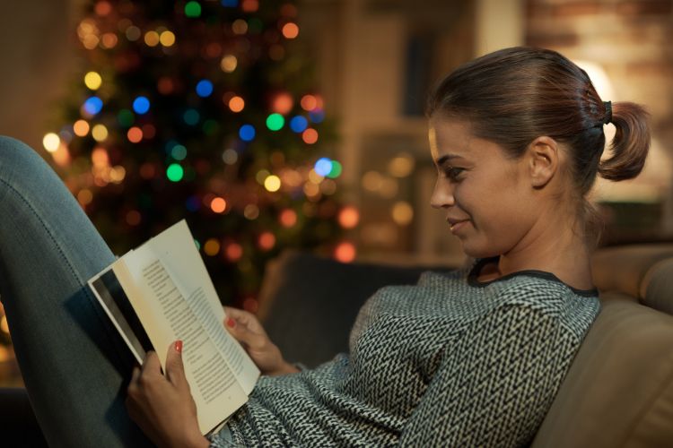 Woman reading book by Christmas lights