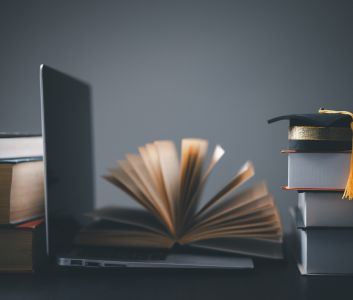 Laptop, open book and mortar board