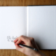 Woman's hand writes 'The End' on the last page of opened sketchbook