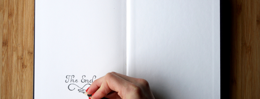 Woman's hand writes 'The End' on the last page of opened sketchbook