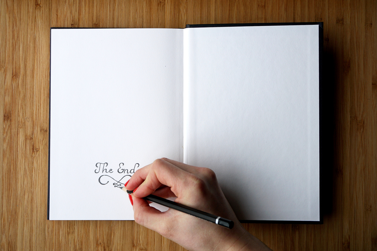 Woman's hand writes 'The End' on the last page of opened sketchbook